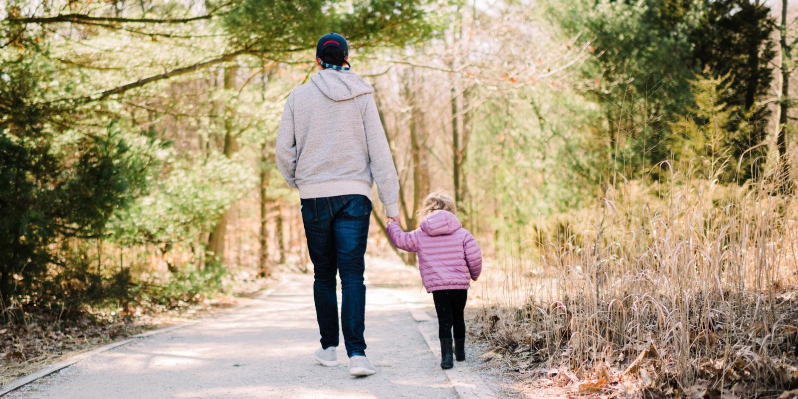 A parent and child walking hand-in-hand away from the camera along a nature trail