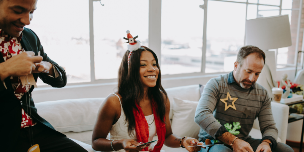 Three adults wearing festive accessories participate in a group activity together in a bright room.