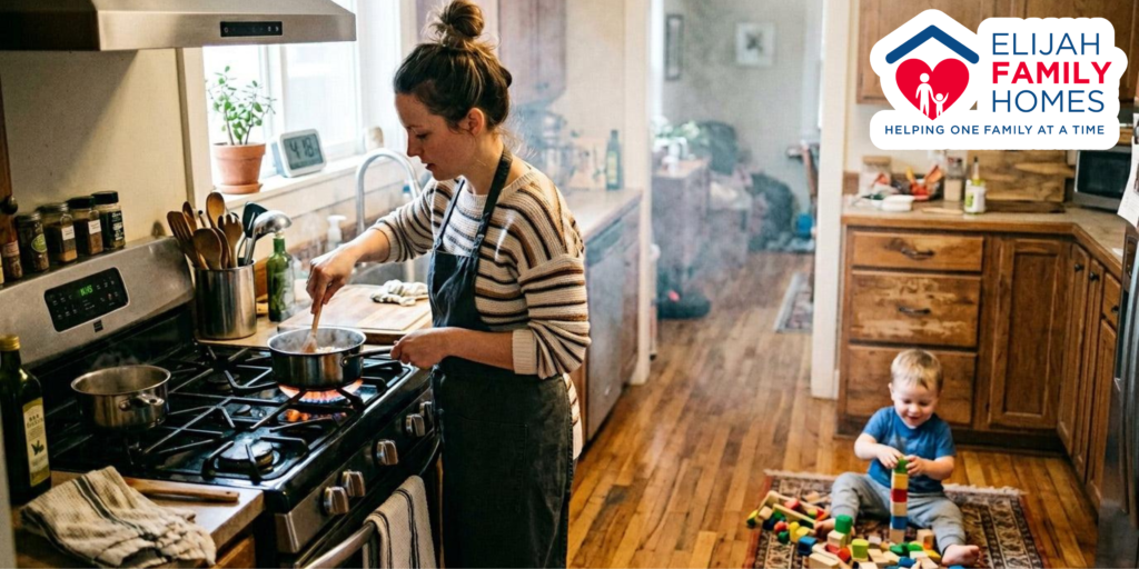 A mother cooking at the stove while her child plays on the ground in the background