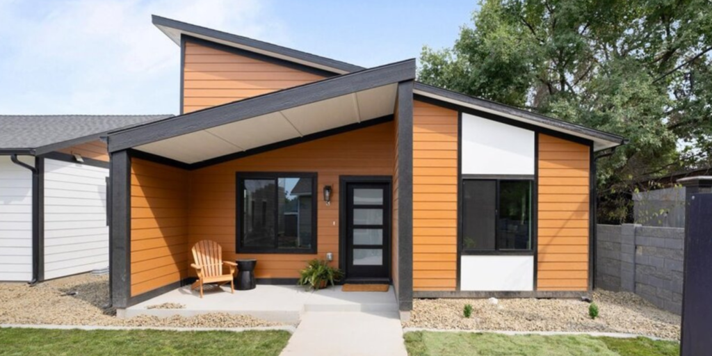 A small modern home with orange siding, a covered porch, and a landscaped front walkway.